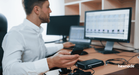 An IT professional in an office carefully monitoring device analytics and working with specialized testing equipment on a desk.